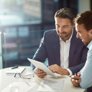 Zwei Geschäftsleute besprechen Unterlagen in einem modernen Büro. Analyse und Beratung zu Headhunter Kosten und Recruiting-Strategien.