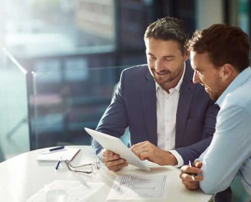 Zwei Geschäftsleute besprechen Unterlagen in einem modernen Büro. Analyse und Beratung zu Headhunter Kosten und Recruiting-Strategien.