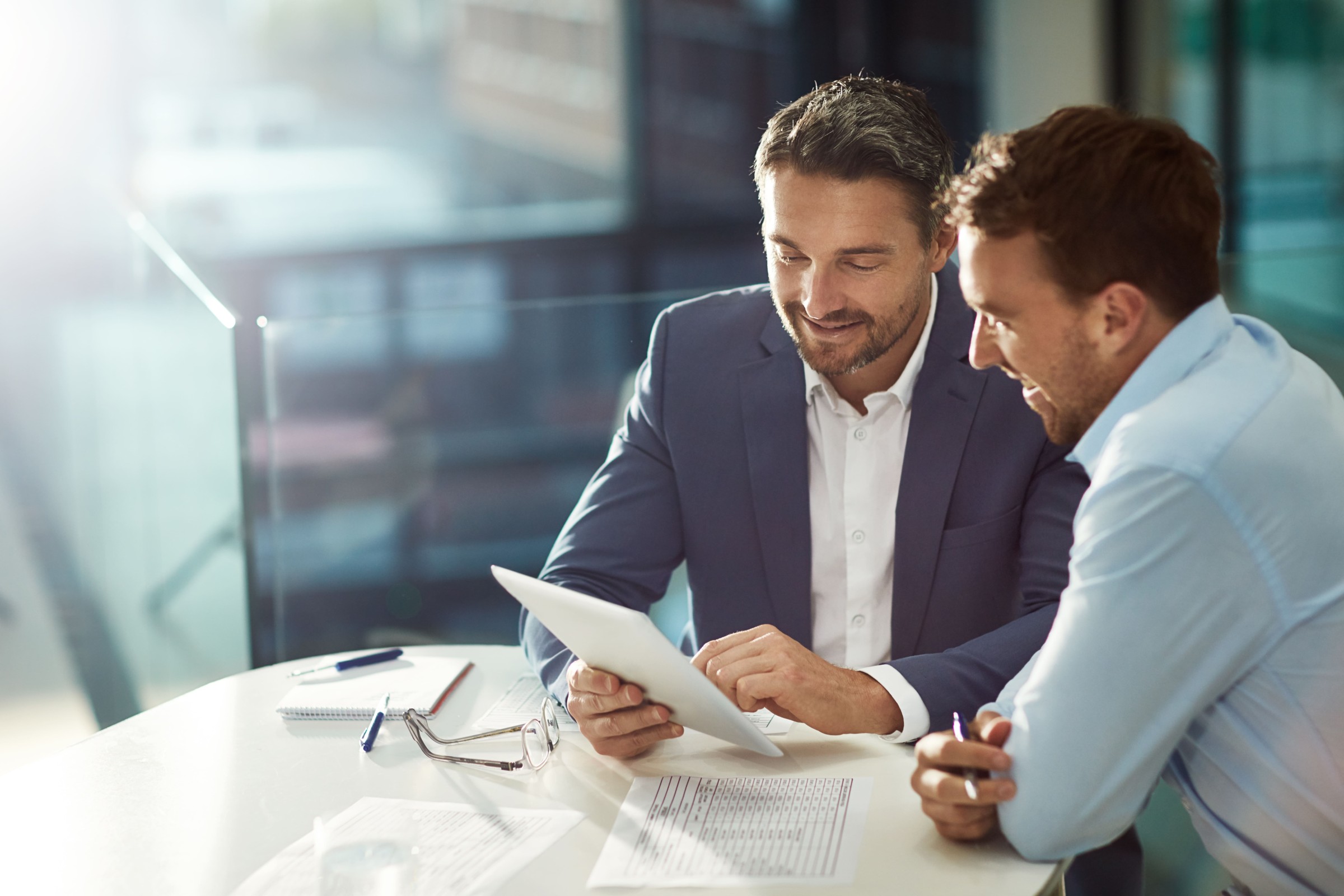 Zwei Geschäftsleute besprechen Unterlagen in einem modernen Büro. Analyse und Beratung zu Headhunter Kosten und Recruiting-Strategien.