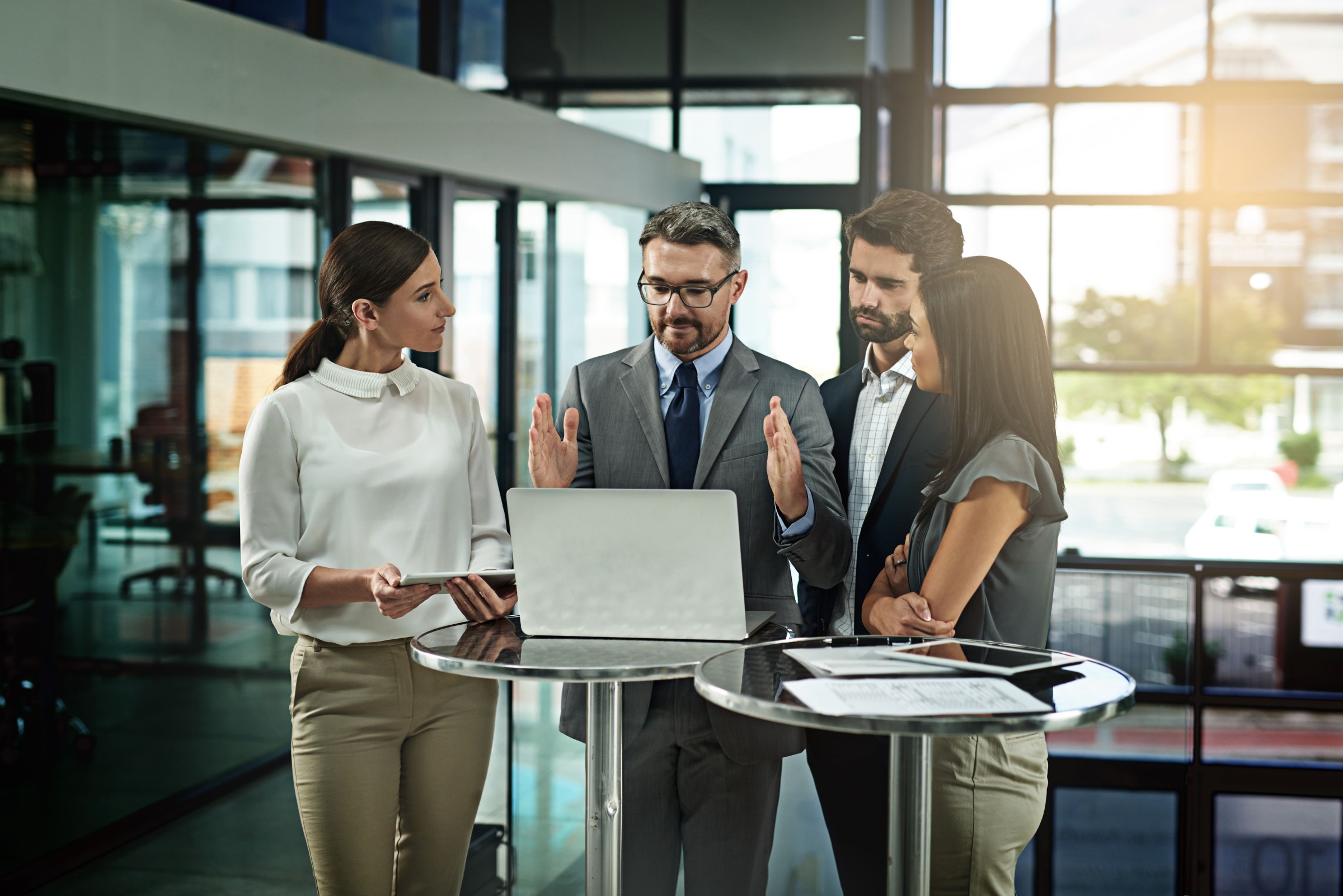 Vier Fachkräfte stehen an einem Stehtisch im Büro und besprechen gemeinsam Ergebnisse an einem Laptop.